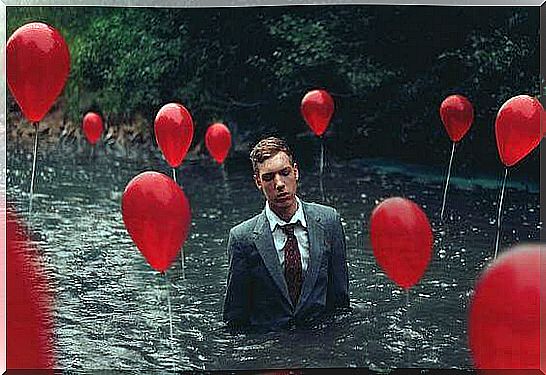 Man in suit in a river surrounded by red balloons